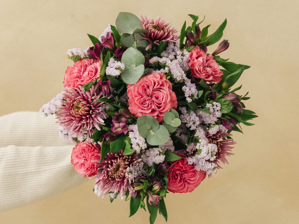 Kanel kraft cardboard flower delivery box held by hand, bouquet stems showing at the base, on a beige background — Mother’s Day flower delivery in Switzerland