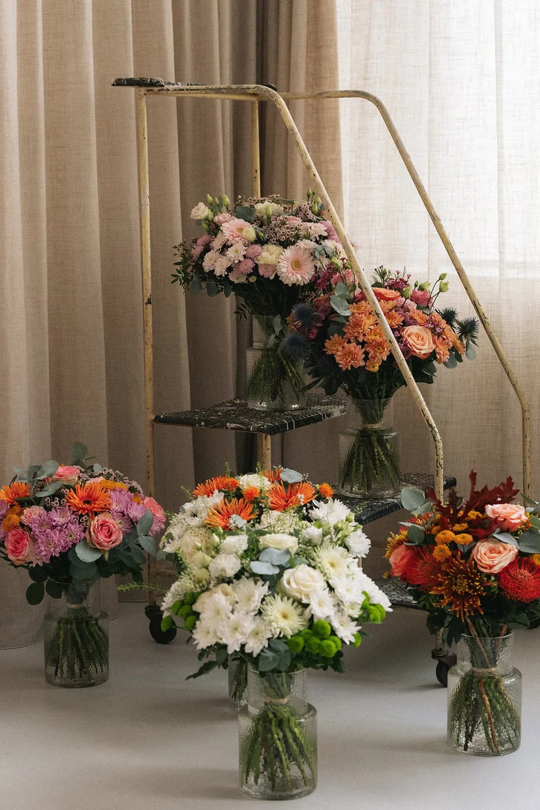 Plusieurs bouquets dans des vases devant un rideau