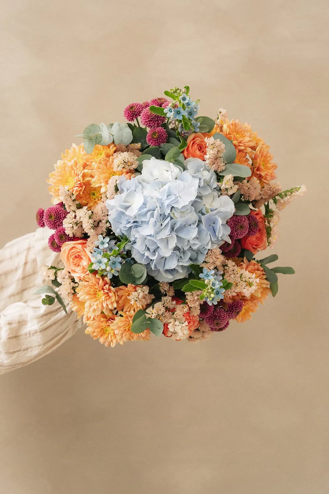 Orange, blue and white bouquet held in two hands