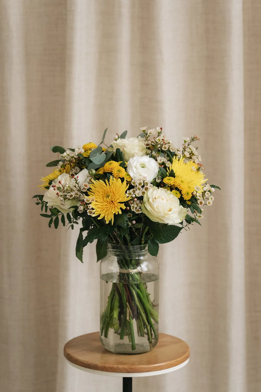 Bouquet jaune et blanc dans un vase devant un rideau