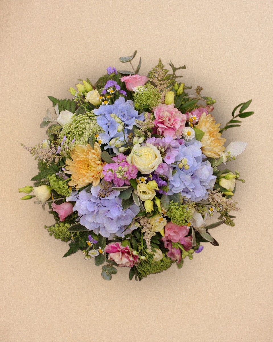 Un bouquet de fleurs colorées composé de roses, d hortensias, de pivoines et de verdure est disposé sur un fond beige.