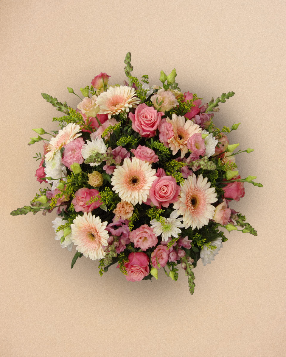 Bouquet rond de fleurs roses et blanches avec des roses, des gerberas et du feuillage, posé contre un fond beige uni.